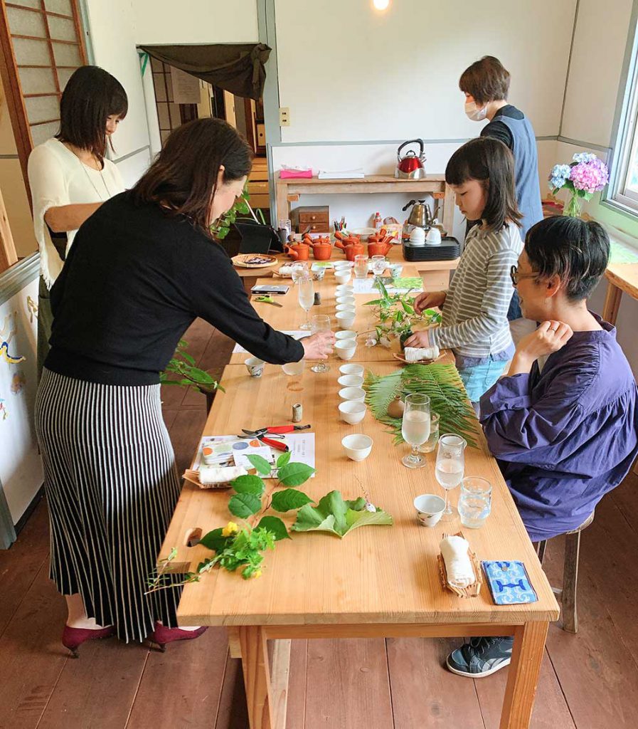 写真：草花とお茶が並んだテーブルを囲む人々