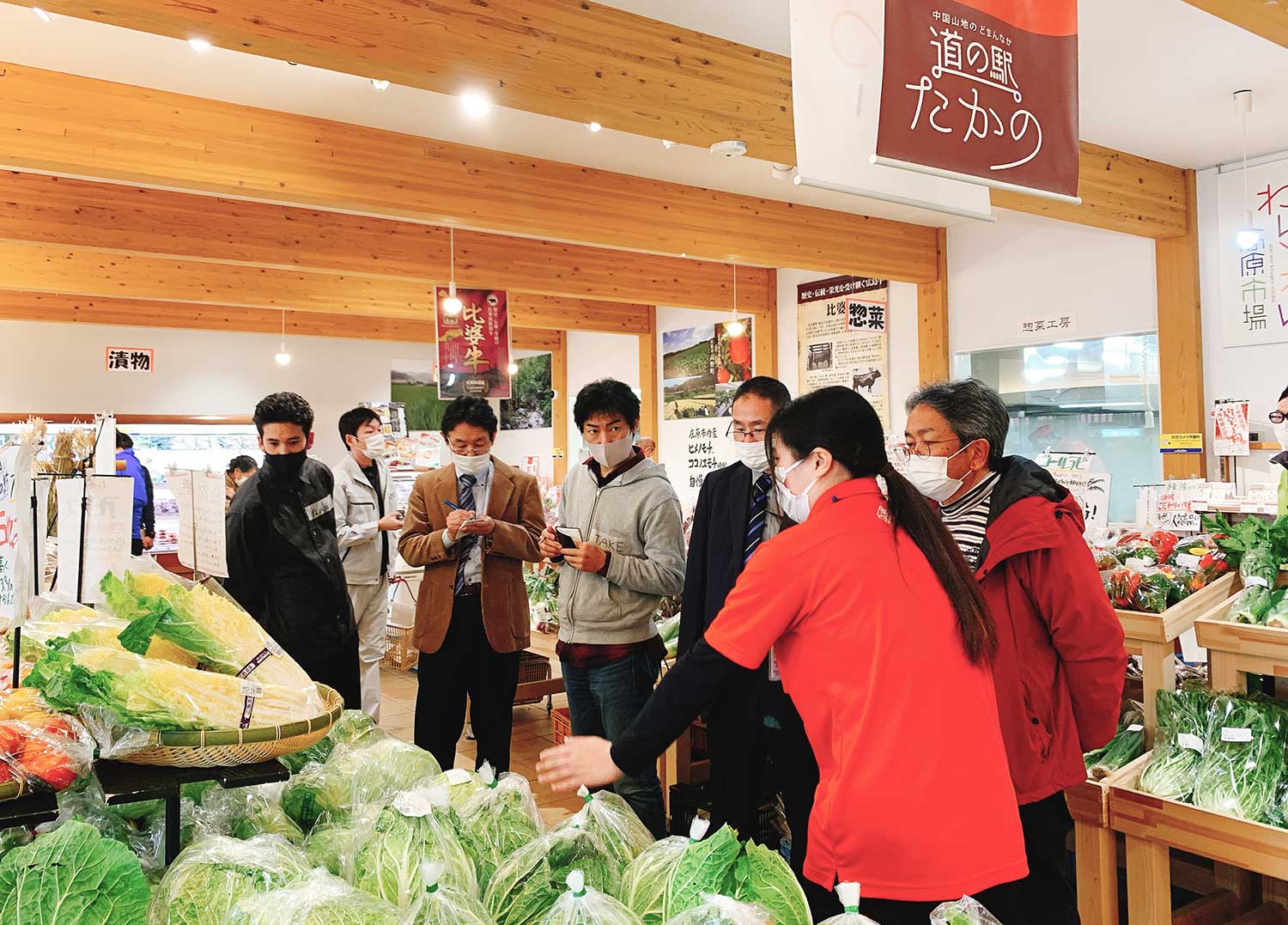 写真：道の駅の野菜売り場でメモを取りながら話を聞く人々